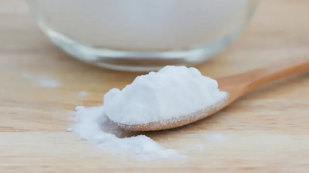 Łyżka z białym proszkiem, który może pomóc na zgagę. W tle szklane naczynie z tym samym produktem.