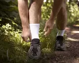 Biegacz przygotowuje się do treningu, sznurując buty. Dobre **jakie skarpetki do biegania** to podstawa komfortu na leśnej ścieżce.