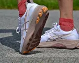 Białe buty do biegania z pomarańczowymi akcentami i charakterystycznym logo. To właśnie asics co to za firma, znana z innowacyjnych rozwiązań dla sportowców.