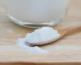 Łyżka z białym proszkiem, który może pomóc na zgagę. W tle szklane naczynie z tym samym produktem.