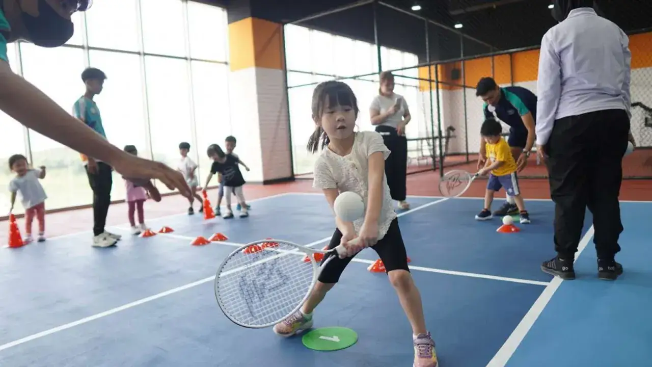 Dzieci uczą się grać w tenis ziemny na kortach, ćwicząc uderzenia i poruszanie się po korcie.