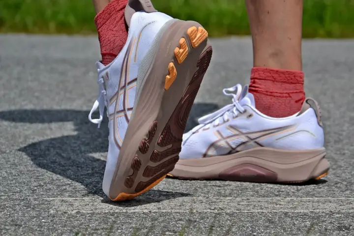 Białe buty do biegania z pomarańczowymi akcentami i charakterystycznym logo. To właśnie asics co to za firma, znana z innowacyjnych rozwiązań dla sportowców.